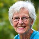 Persona de edad avanzada sonriendo y haciendo yoga en un parque, con un aura de vitalidad y buena salud.